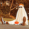 A sheet ghost sitting and wearing sunglasses, a crown, and sneakers